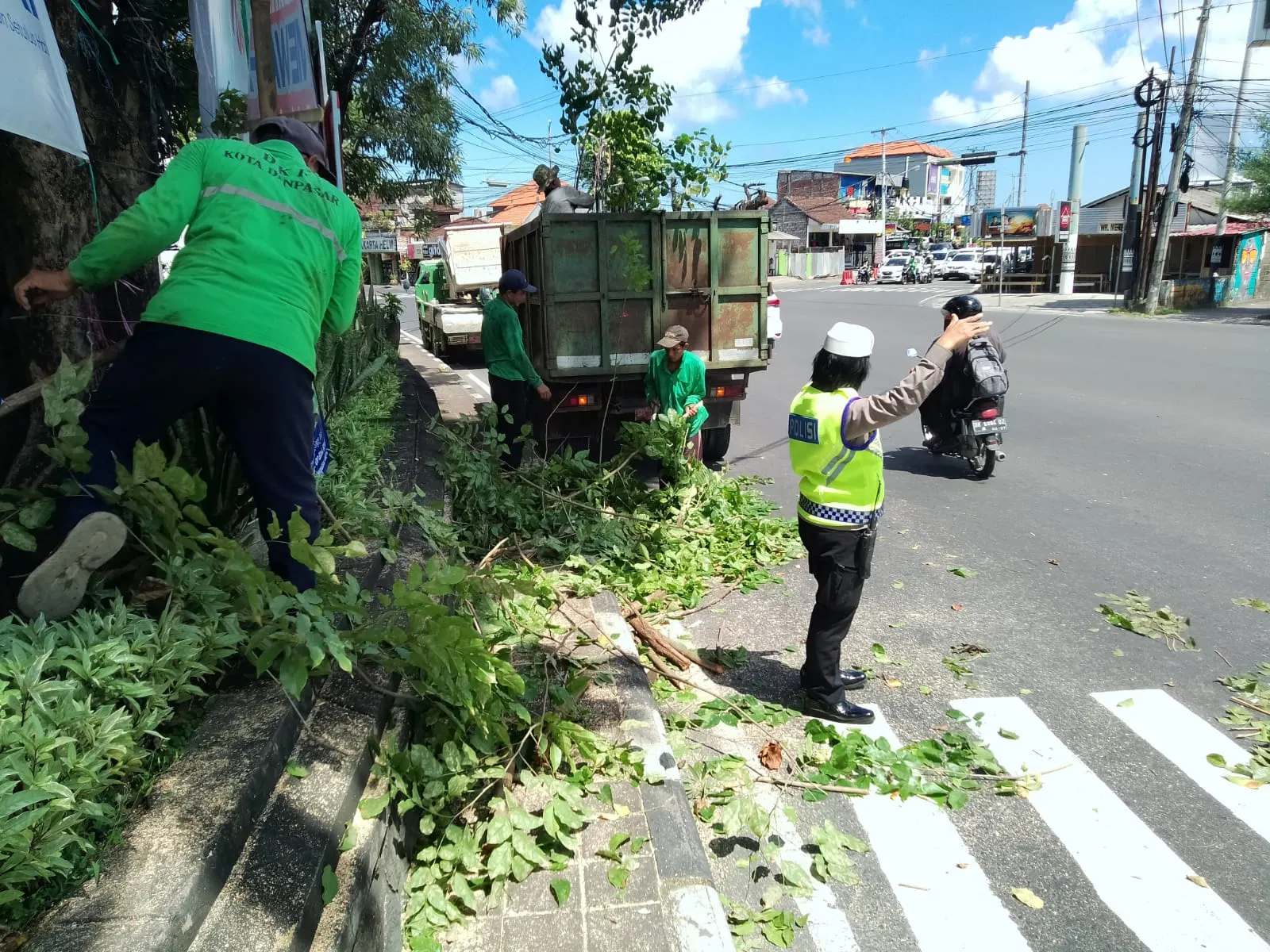 Disaat DKP Lakukan Pemangkasan Pohon Tepi Jalan, Kanit Lantas Polsek Denpasar Barat Pengaturan Lalin Untuk Keamanan Pengguna Jalan